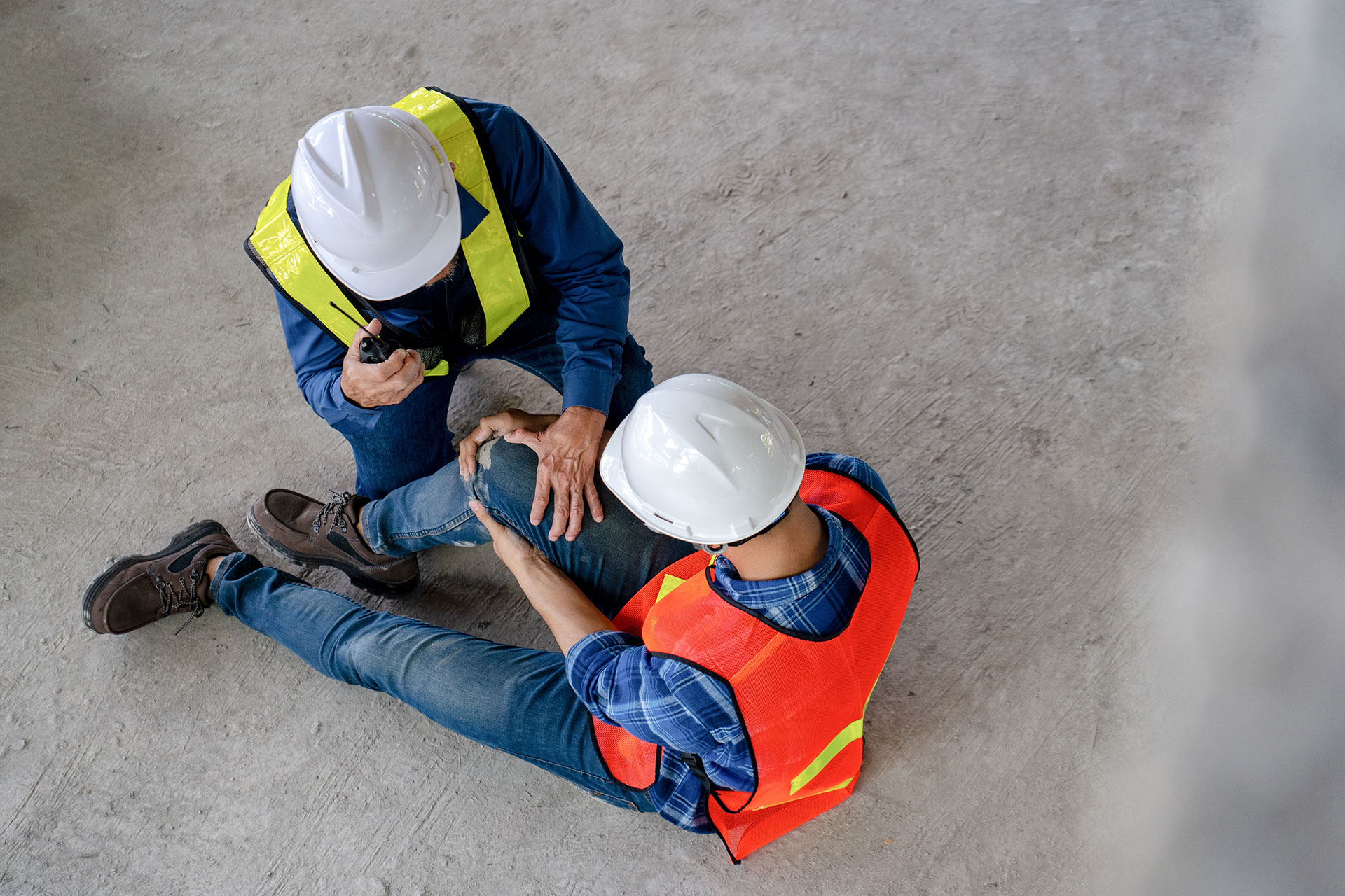 Industrial worker injured holding knee while other worker is talking in walkie-talkie
