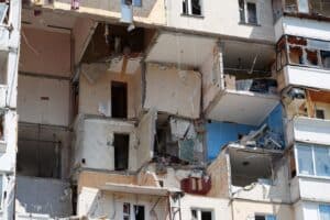 Partially demolished apartment building with exposed rooms, broken walls, hanging wires, and debris visible across multiple floors.